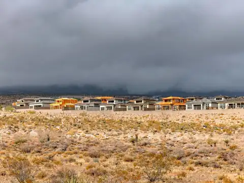 Dark storm clouds low over a row of stucco houses at the edge of open desert scrub