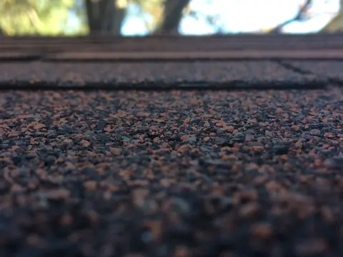 Red-brown and black mineral granules on the surface of asphalt shingles, seen close up